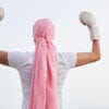 Unrecognizable female cancer patient with pink headscarf and boxing gloves in her hands as a sign of fight and strength. Concept of fighting and beating cancer.