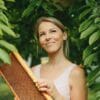 Young woman outdoors standing among some low hanging branches, smiling and holding a frame from a beehive - source of many of the ingredients used in Unbeelievable Health natural supplements